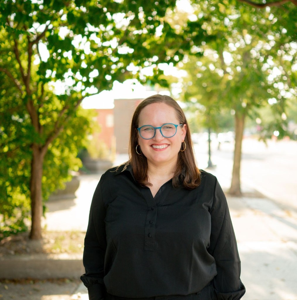 photo of a woman in a black shirt and blue glasses surrounded by trees